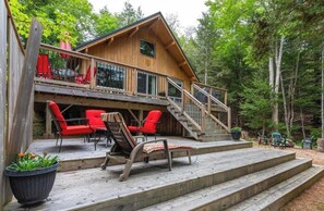 Eine Holzhütte mit einer Terrasse, Sitzgelegenheiten im Freien und einer Treppe, die zum oberen Stockwerk führt.