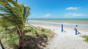 A beach with a palm tree, a sandy path, and a clear view of the ocean. - Casa c 5 su tes Piscina Churrasqueira e Sinuca (Cabedelo)