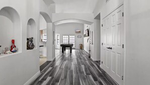 A hallway with a dark wood floor, white walls, and arched doorways. There is a pool table in the center. - 3BR Spacious Scottsdale Home w/ Hot Tub & Pool! (Scottsdale)
