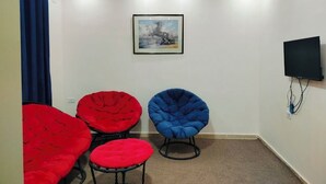 A room with three bean bag chairs, one red and two blue, a mounted TV, and a framed picture on the wall. - Petra Heaven Botique (Wadi Musa)