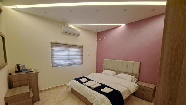 A bedroom with a bed, bedside tables, a desk, and a window with blinds. - Petra Heaven Botique (Wadi Musa)