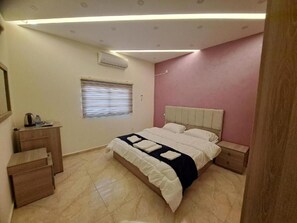 A bedroom with a bed, bedside tables, a desk, and a window with blinds. - Petra Heaven Botique (Wadi Musa)