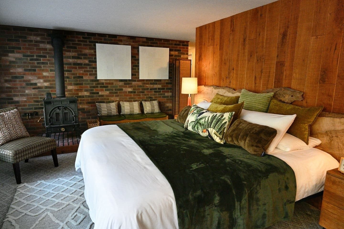 Une chambre avec un mur en briques, un lit avec de nombreux oreillers, un banc avec des coussins et une tête de lit en bois.