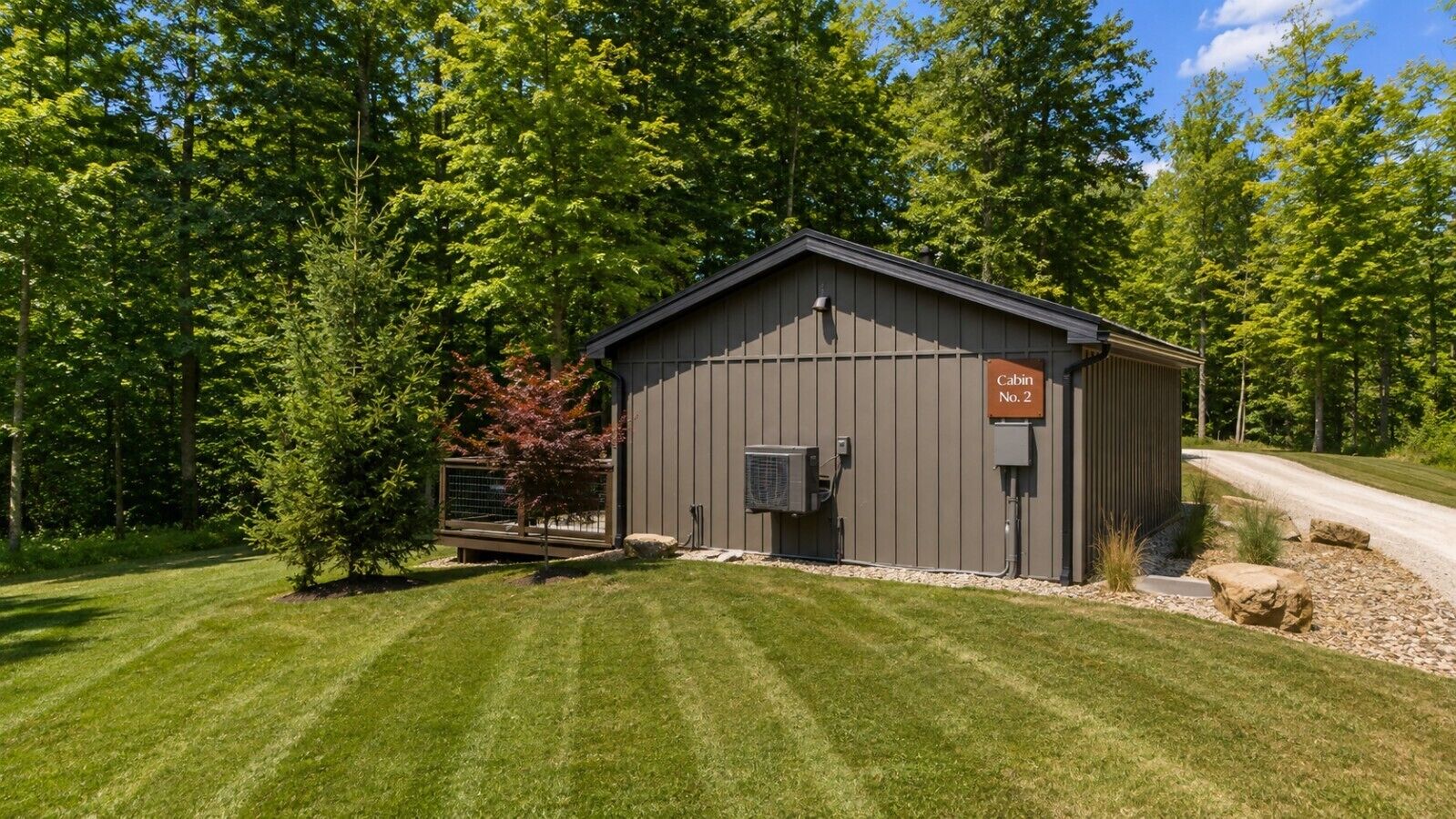 A cabin with a metal exterior, a sign indicating 'Cabin No. 2', and a paved driveway leading to it.