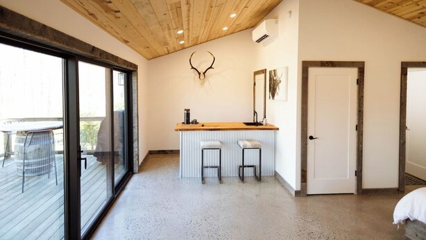 A room with a wooden ceiling, a bar area with stools, a large mirror, and a door.