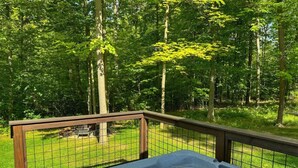 A hot tub on a wooden deck with a metal railing, surrounded by a grassy yard and trees.