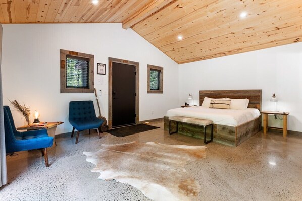 Un dormitorio con techo de madera, una cama con cabecera de madera, una silla azul, un banco y una alfombra de cuero de vaca.