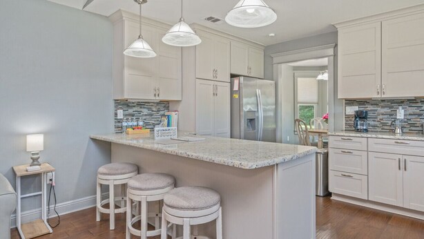A kitchen with white cabinets, a marble island, bar stools, pendant lights, and a refrigerator. - Private Pool • 3BR Family Fun Home w/ Gazebo (Crestview)