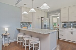 A kitchen with white cabinets, a marble island, bar stools, pendant lights, and a refrigerator. - Private Pool • 3BR Family Fun Home w/ Gazebo (Crestview)