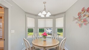 A dining area with a round table, chairs, a chandelier, and a view through large windows. - Private Pool • 3BR Family Fun Home w/ Gazebo (Crestview)