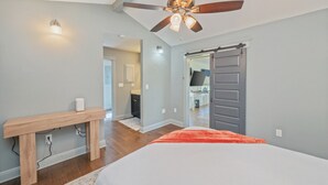 A bedroom with a bed, a ceiling fan, a wooden bench, and a door leading to a bathroom. - Private Pool • 3BR Family Fun Home w/ Gazebo (Crestview)