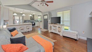 A spacious living area with a grey sofa, ottoman, and a television on a cabinet. - Private Pool • 3BR Family Fun Home w/ Gazebo (Crestview)