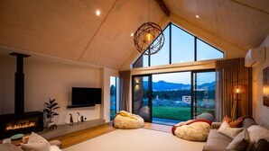 A spacious living room with a fireplace, comfortable seating, and large windows offering a view of the outdoors.