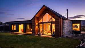 A modern house with a large glass front, a stone exterior, and a well-maintained lawn.