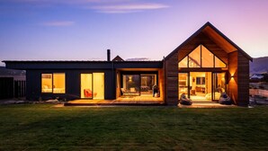 A modern two-story house with large glass windows, a wooden deck, and a well-maintained lawn.