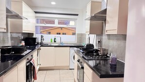 A modern kitchen with black countertops, stainless steel appliances, and a window with a view of a building. - Room 1: A Bright and Spacious Double Bed With En-Suite, Ilford, London, UK (Ilford)