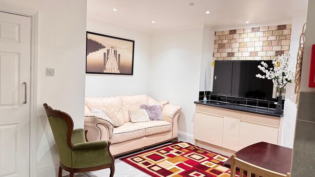 A living room with a beige sofa, a green armchair, a patterned rug, and a large TV. - Room 1: A Bright and Spacious Double Bed With En-Suite, Ilford, London, UK (Ilford)