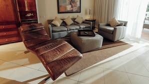 A modern living room with a leather sofa, a grey armchair, and a matching ottoman. There is a coffee table, a side table, and a painting on the wall.