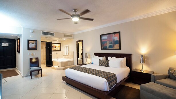 A hotel room with a large bed, a ceiling fan, a bathroom with a bathtub, and a seating area with a chair and a table.