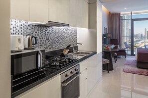 A modern kitchen with a gas stove, microwave, and kettle, and a dining area with a view of the city. - Damac Maison Aykon City Dubai (Dubai)