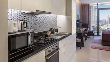 A modern kitchen with a microwave, stove, and kettle, a dining area with a table and chairs, and a large window offering a city view.
