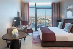 A modern hotel room with a large bed, a desk, and a view of a cityscape through floor-to-ceiling windows. - Damac Maison Aykon City Dubai (Dubai)