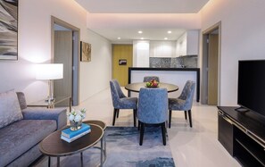 A modern living room with a sofa, coffee table, and TV. There is a dining area with a table and chairs. The room has a kitchen in the background. - Damac Maison Aykon City Dubai (Dubai)