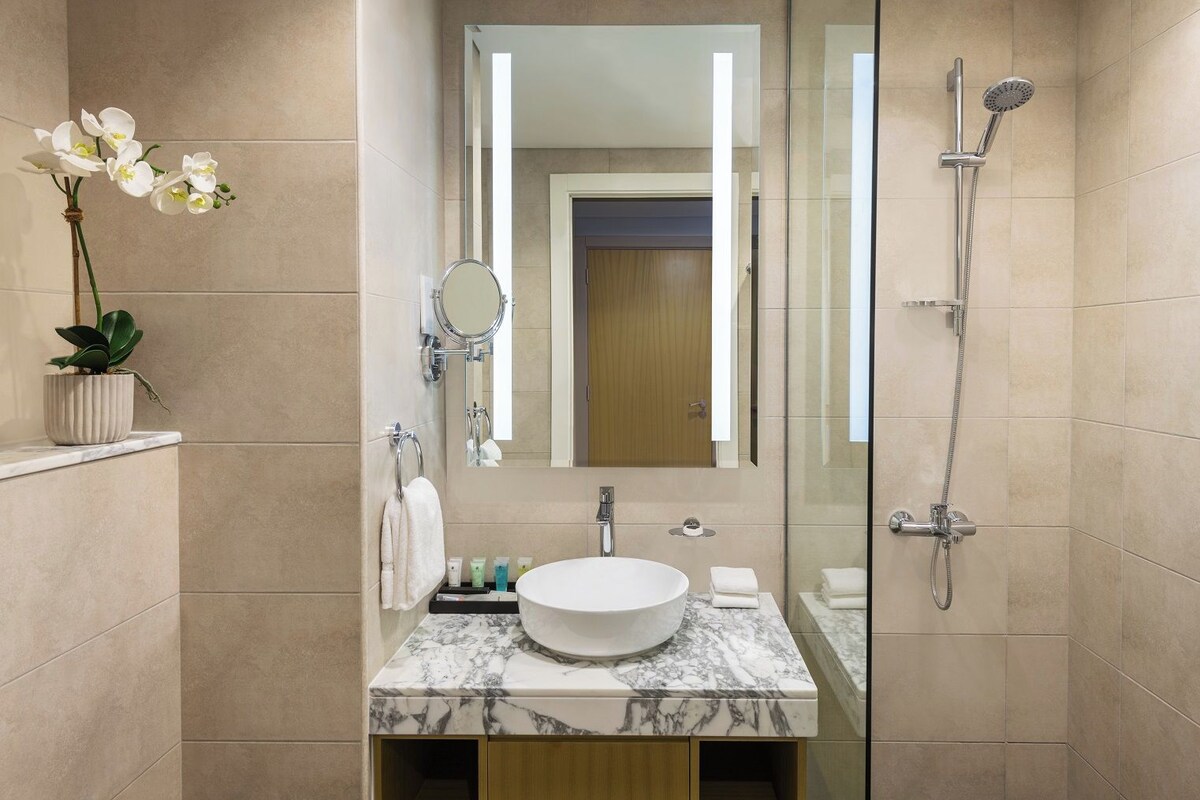 A modern bathroom with a marble sink, a glass-enclosed shower, and a potted orchid.