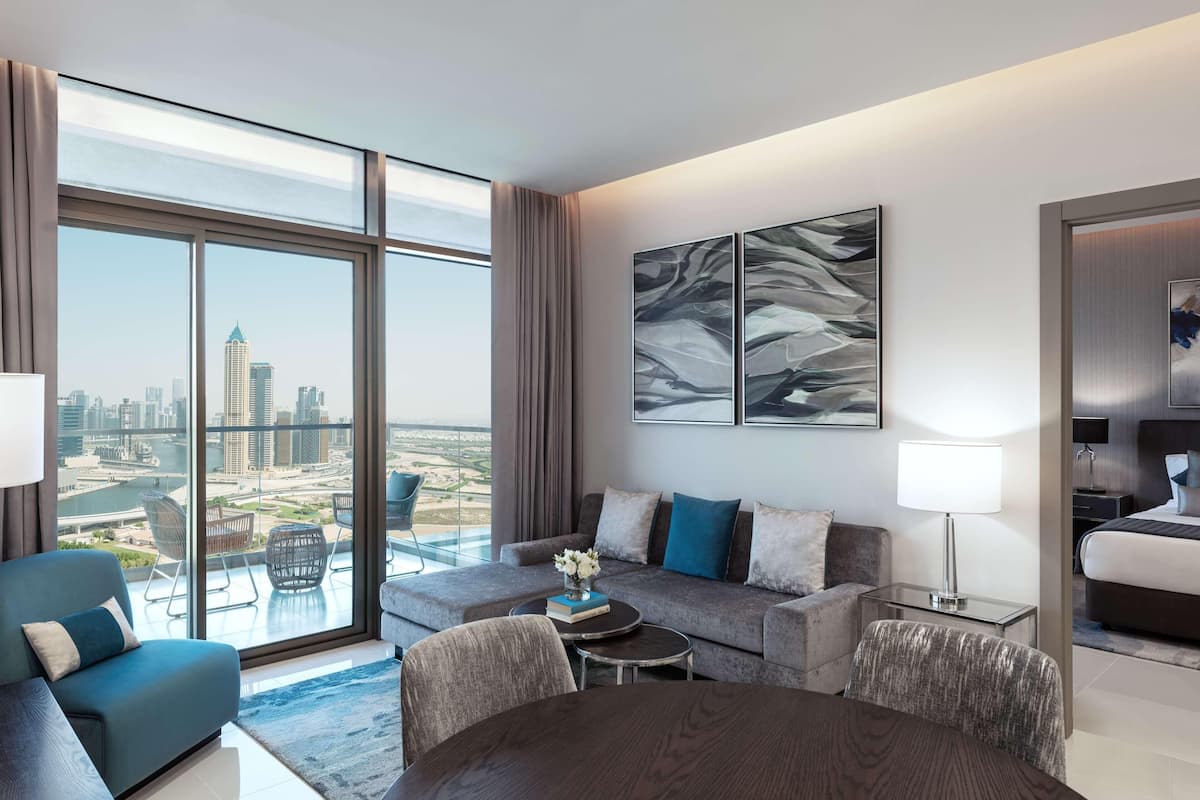 Habitación de hotel moderna con un amplio ventanal que ofrece vistas a la ciudad, un sofá, una mesa de comedor y una cama.
