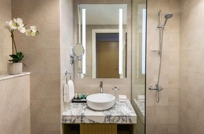 A modern bathroom with a marble vanity, a large mirror, a handheld showerhead, and a potted orchid. - Damac Maison Aykon City Dubai (Dubai)