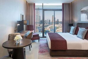 A modern hotel room with a large bed, a desk, a chair, and a view of a cityscape through large windows. - Damac Maison Aykon City Dubai (Dubai)