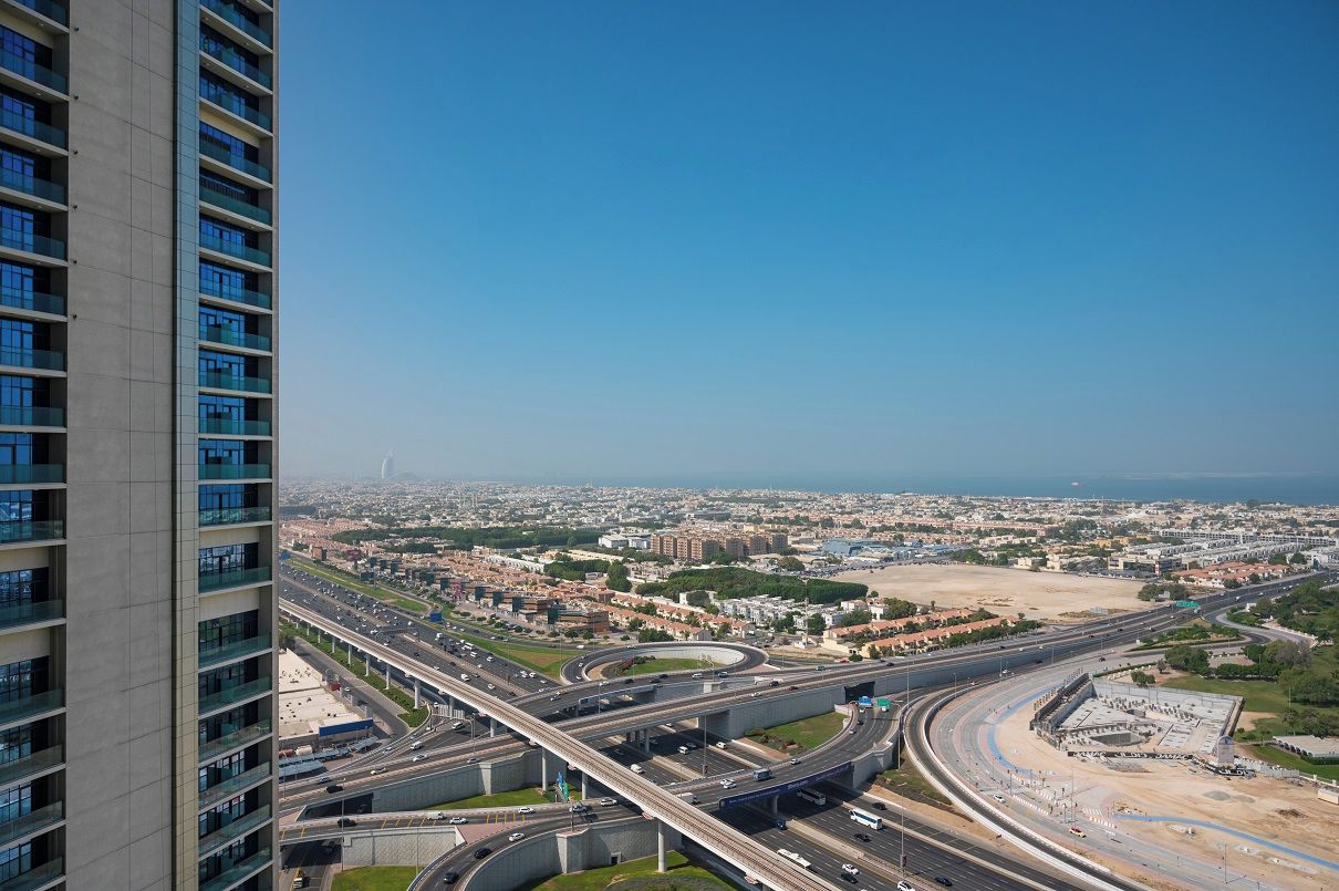 A high-rise building with multiple floors and large windows, overlooking a cityscape with a highway and a large open area.