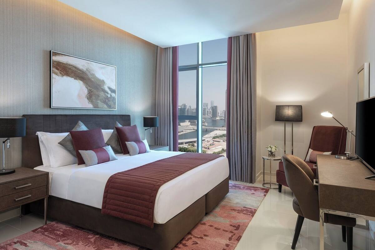 A modern hotel room with a large bed, a desk, a chair, and a TV.