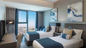 Habitación de hotel con dos camas, un escritorio y un amplio ventanal con vistas a la ciudad.