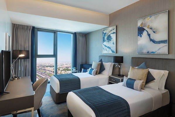 Une chambre d’hôtel avec deux lits, un bureau et une grande fenêtre donnant sur la ville.