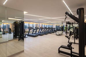 Une salle de sport moderne équipée de nombreux tapis de course, d’appareils de musculation et d’un grand miroir qui reflète le paysage urbain.