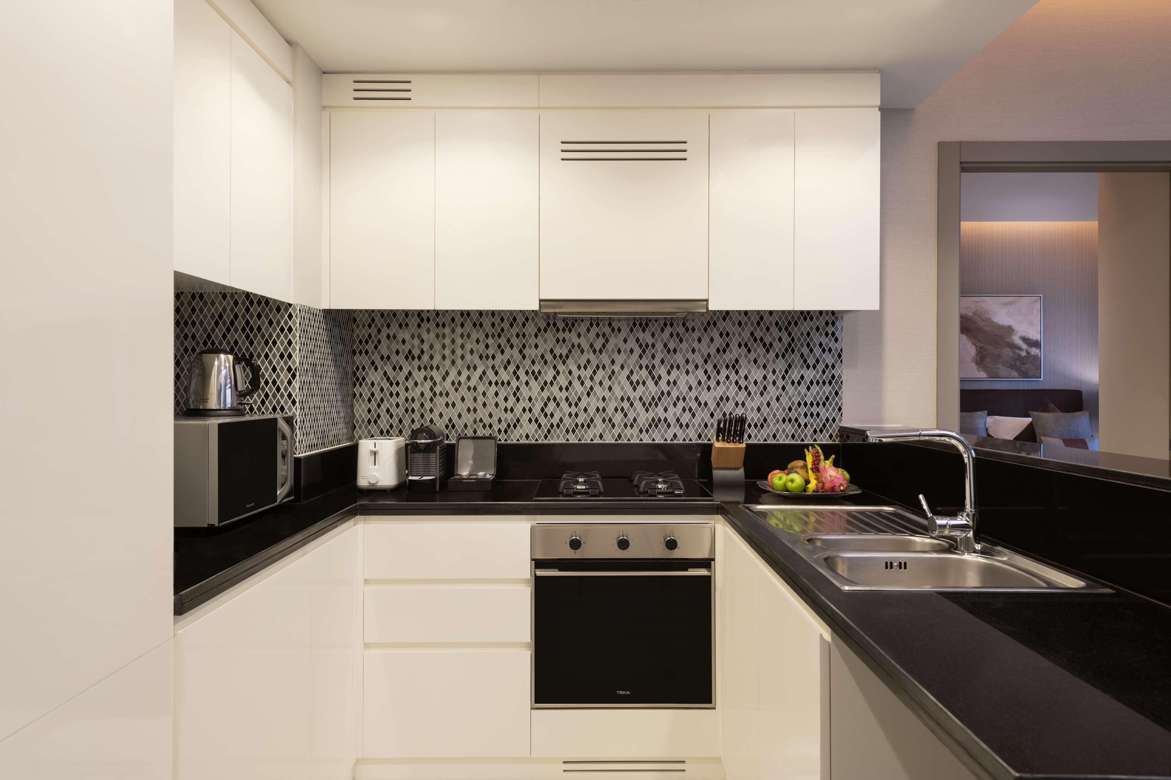 A modern kitchen with white cabinets, a black countertop, a stainless steel microwave, a toaster, a stove, and a sink.