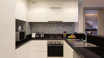 A modern kitchen with white cabinets, a black countertop, a stainless steel microwave, a toaster, a stove, and a sink.