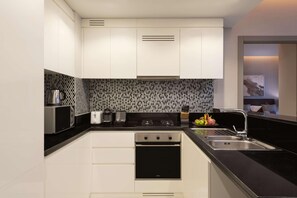 A modern kitchen with white cabinets, a black countertop, a stainless steel microwave, a toaster, a stove, and a sink. - Damac Maison Aykon City Dubai (Dubai)