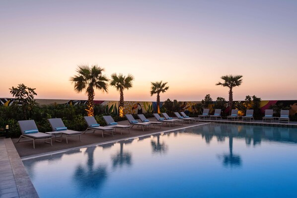 A poolside area with lounge chairs and palm trees against a sunset backdrop. - Damac Maison Aykon City Dubai (Dubai)