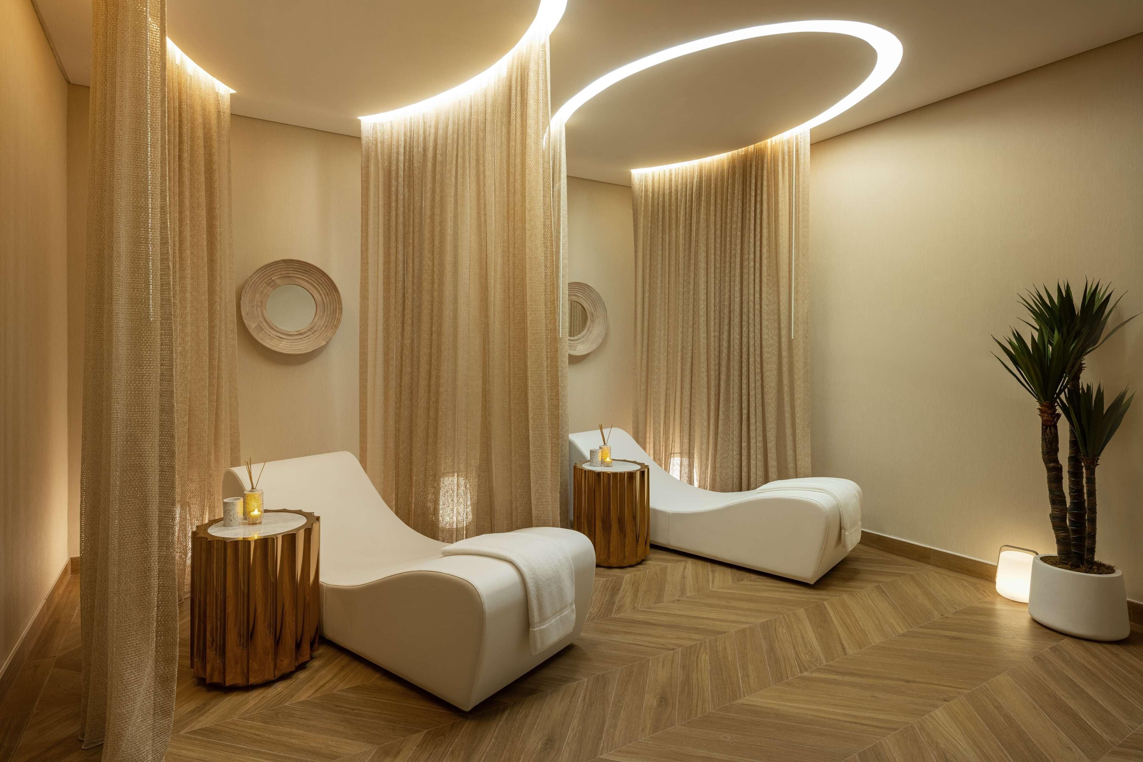 Une salle de spa moderne avec deux fauteuils inclinables, des tables d’appoint en bois et une plante en pot.