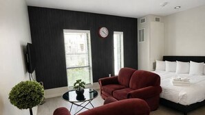 A modern hotel room with a bed, two red armchairs, a small table with a plant, and a wall-mounted clock. - Affordable Classy Studio in Downtown Des Moines! (Des Moines)