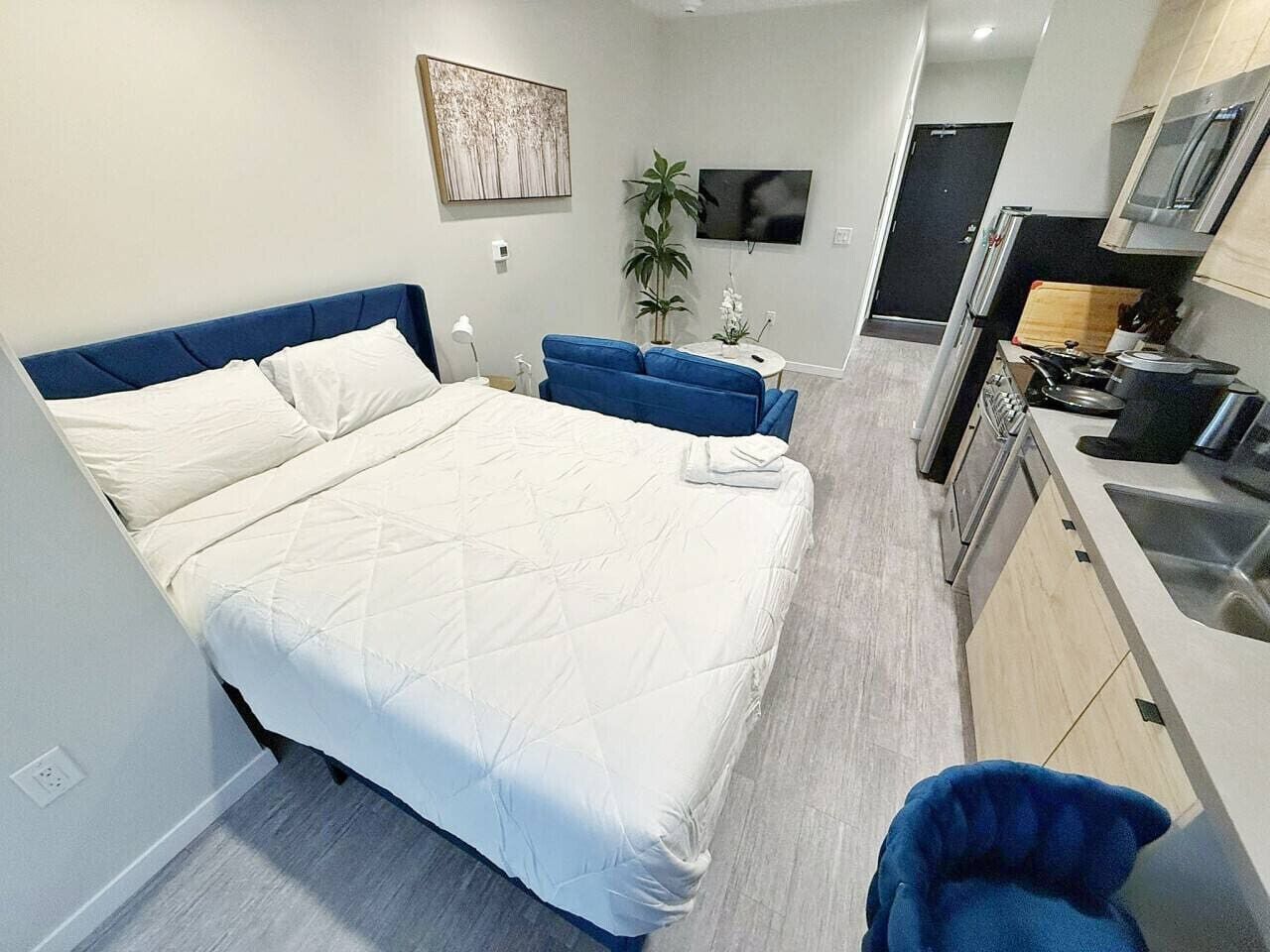 Una habitación de hotel moderna con una cama grande, un pequeño espacio para sentarse, una kitchenette y un televisor fijado a la pared.