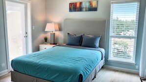 Ein Schlafzimmer mit einem Bett, einem Nachttisch, einer Lampe, einem Gemälde und einem Fenster mit Jalousien.