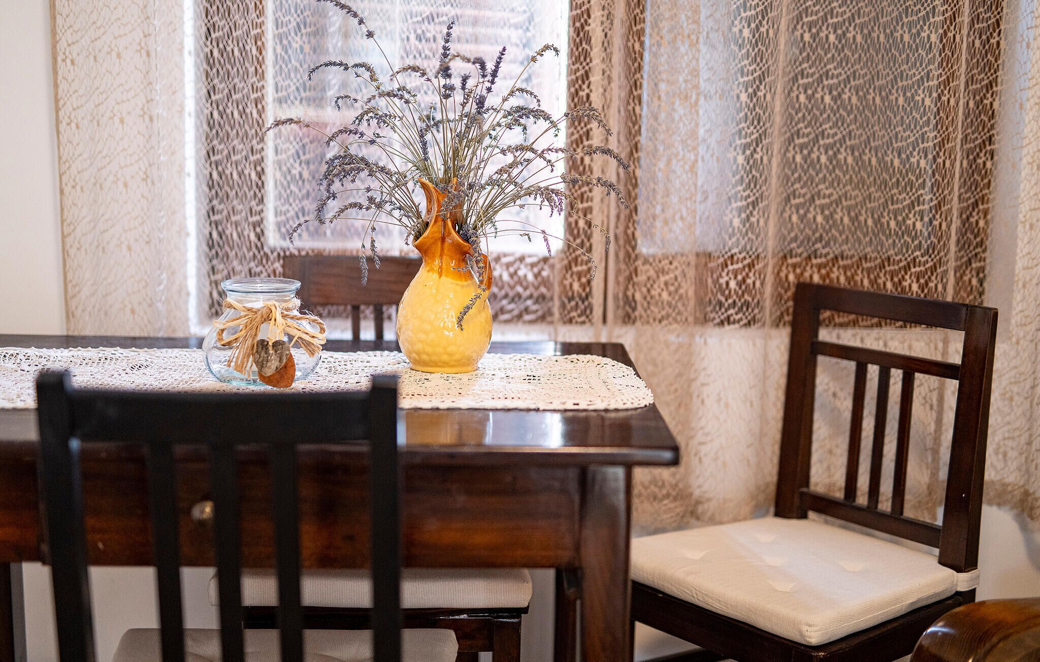 Une table à manger ornée d’un vase de fleurs séchées et d’un bocal en verre décoré d’un motif en forme de cœur.