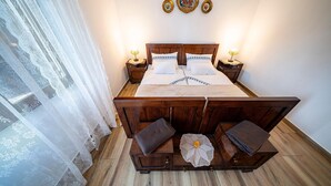 A wooden bed with white linens, two bedside tables with lamps, a lace curtain, and a wall-mounted decorative plate. - Stunning home in Slatinski Drenovac (Slatinski Drenovac)