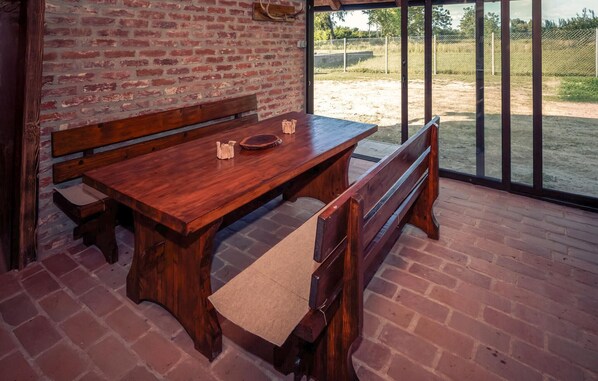A wooden table with benches in a room with brick walls and large windows.