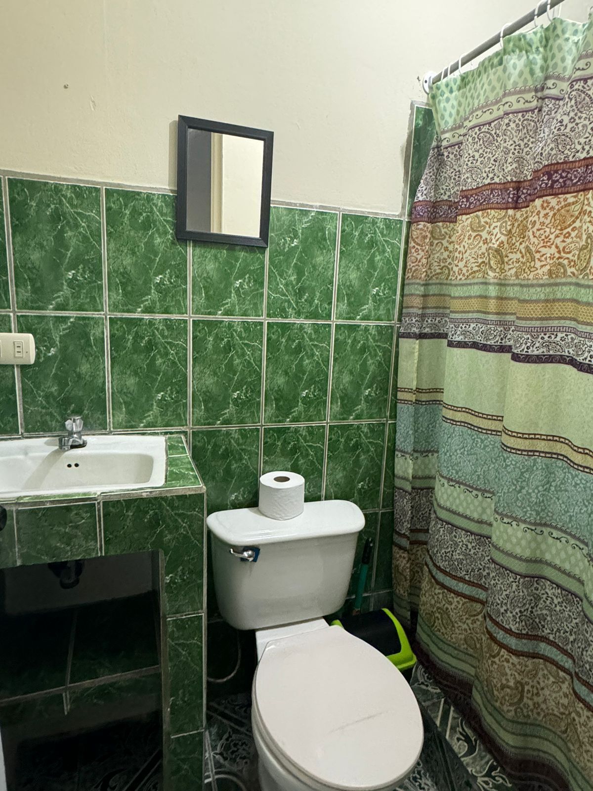 A bathroom with green marble tiles, a white sink, a toilet, and a patterned shower curtain.