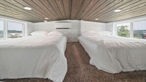 Un dormitorio con dos camas, vigas de madera en el techo y grandes ventanales con vistas al exterior.