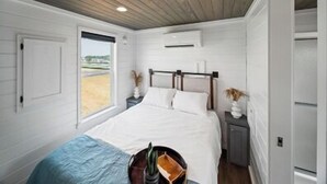 Un dormitorio con techo de madera, cama con ropa de cama blanca, mesita de noche pequeña y ventana con vistas al exterior.